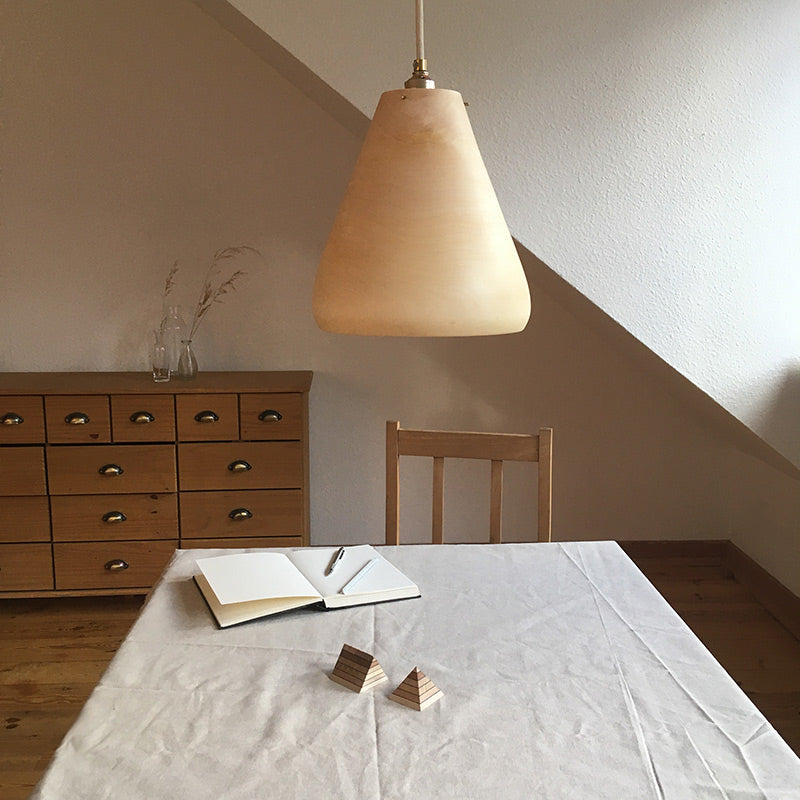 Holzlampe hängt über einem Wohnzimmertisch mit Tischdecke und Buch
